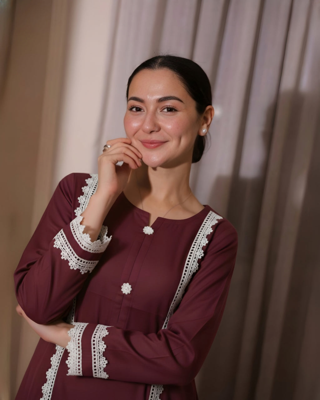 Woman wearing a maroon dress with white lace details against a beige curtain background