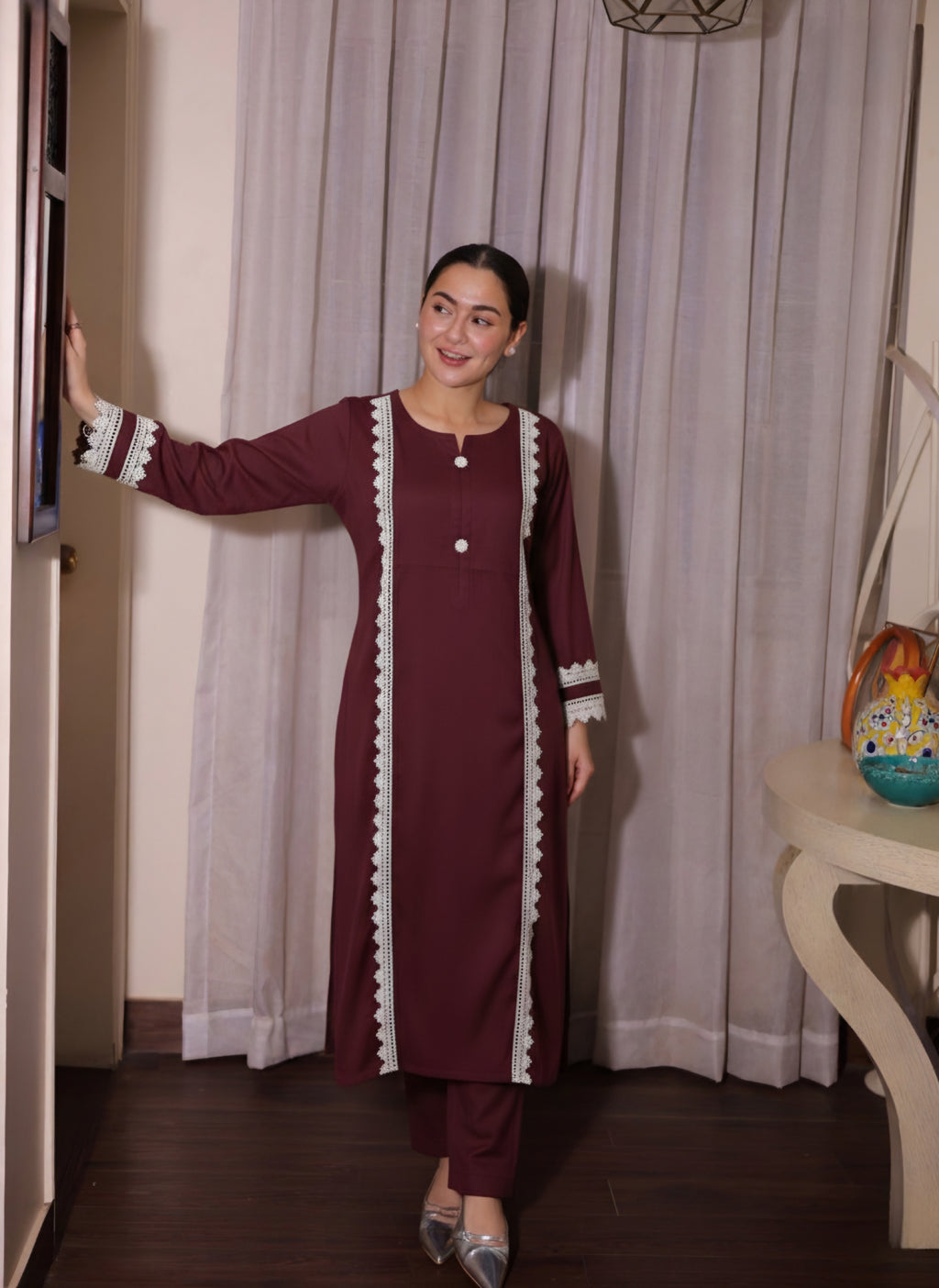 Woman wearing a maroon traditional outfit with white patterns in a room.